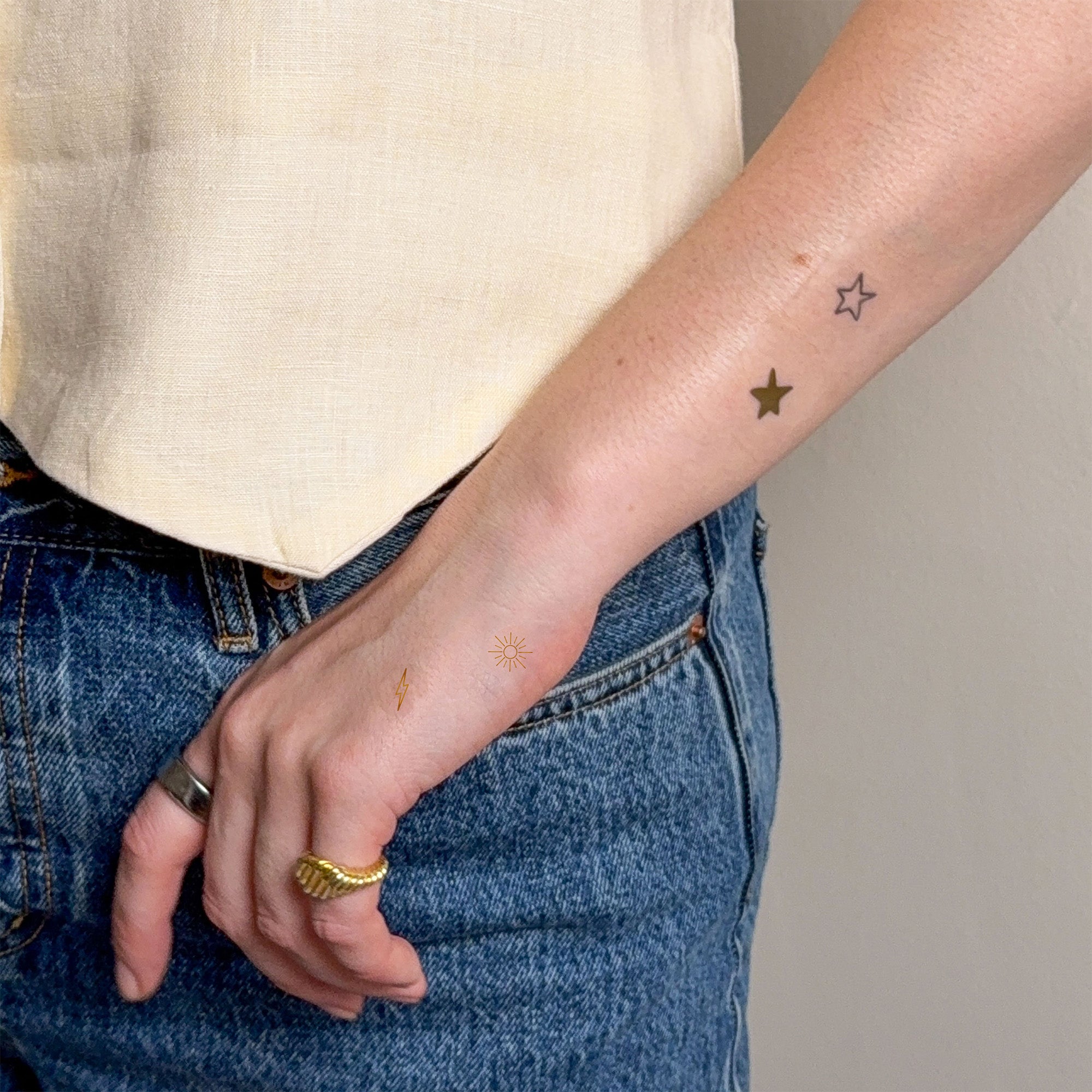 Person wearing blue jeans and a beige top with patches on their arm and hand.
